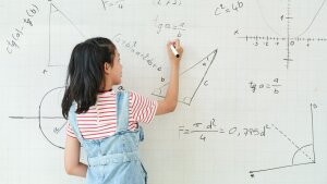 Kind steht vor einer Tafel und schreibt Formeln