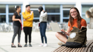 Eine junge Studentin sitz auf dem Campus am Laptop