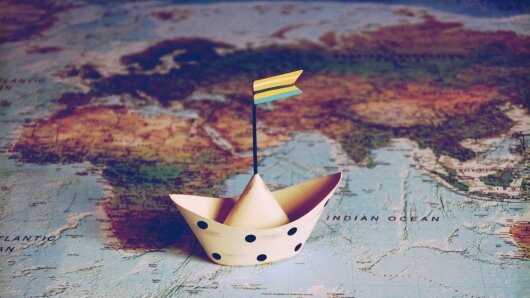 Papierschiff segelt auf einer Weltkarte